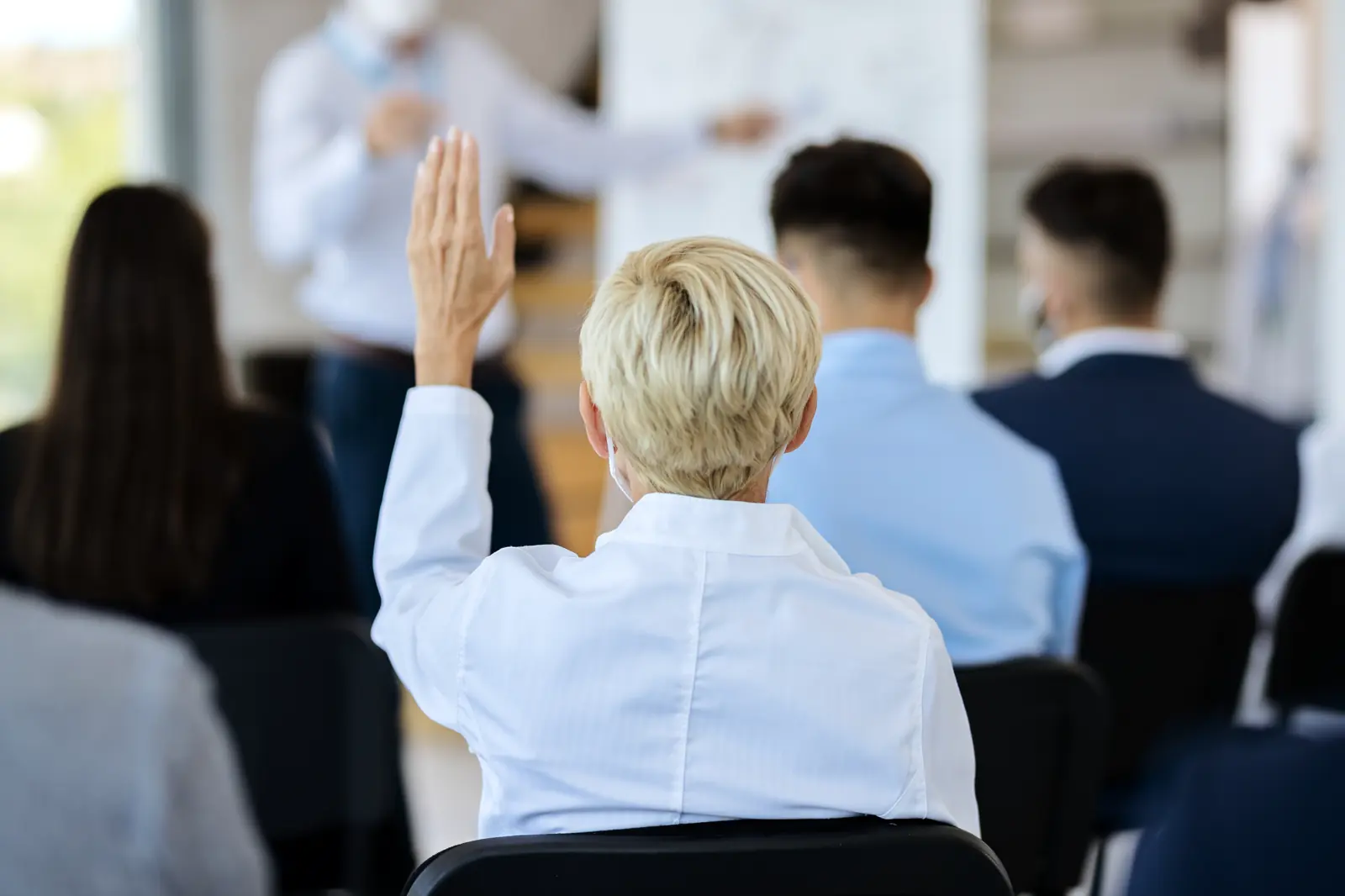 Seminarteilnehmende von hinten, eine Person meldet sich mit erhobener Hand