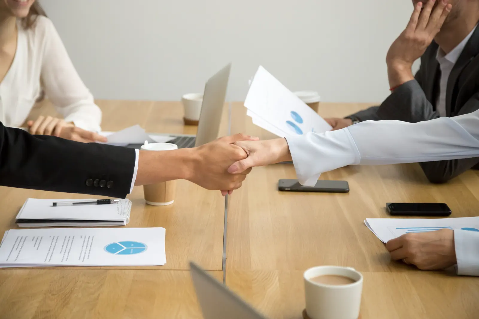 Handschlag über einem Besprechungstisch mit Unterlagen